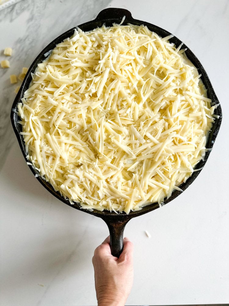 gratin dauphinois au fromage pas encore cuit, recouvert de fromage râpé dans une grande casserole en fonte