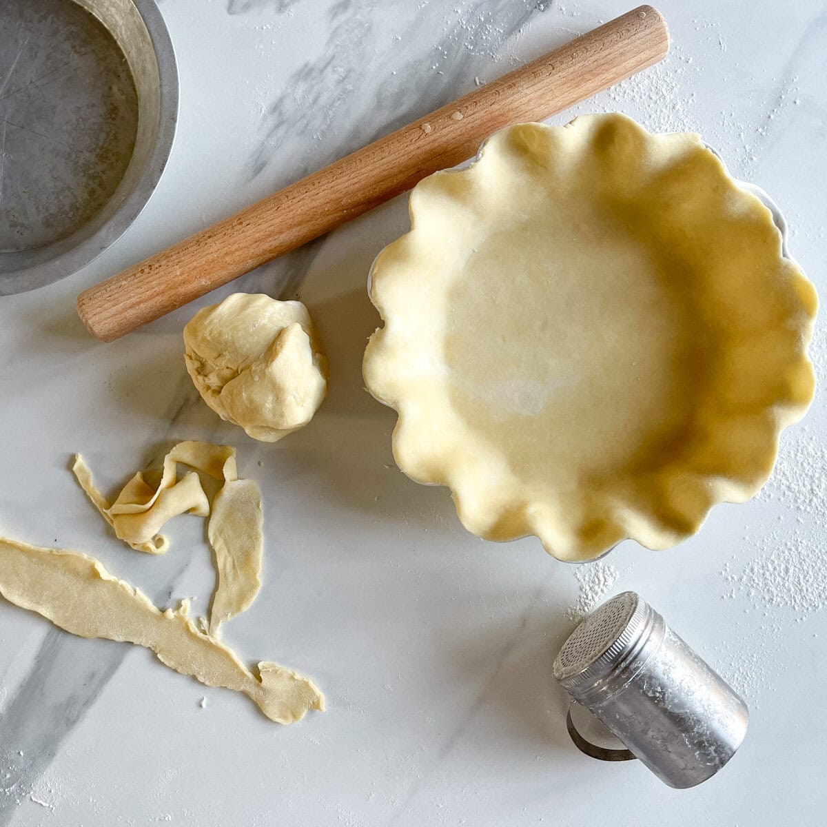 pâte à tarte maison dans un moule sur comptoir avec retaille farine et rouleau à pâtisserie