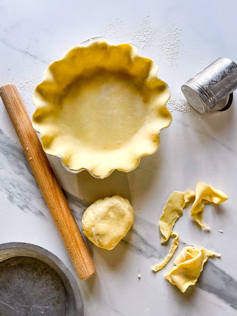 pâte à tarte dans moule à tarte sur comptoir blanc avec reste de pâte ,rouleau à pâtisserie et retailles
