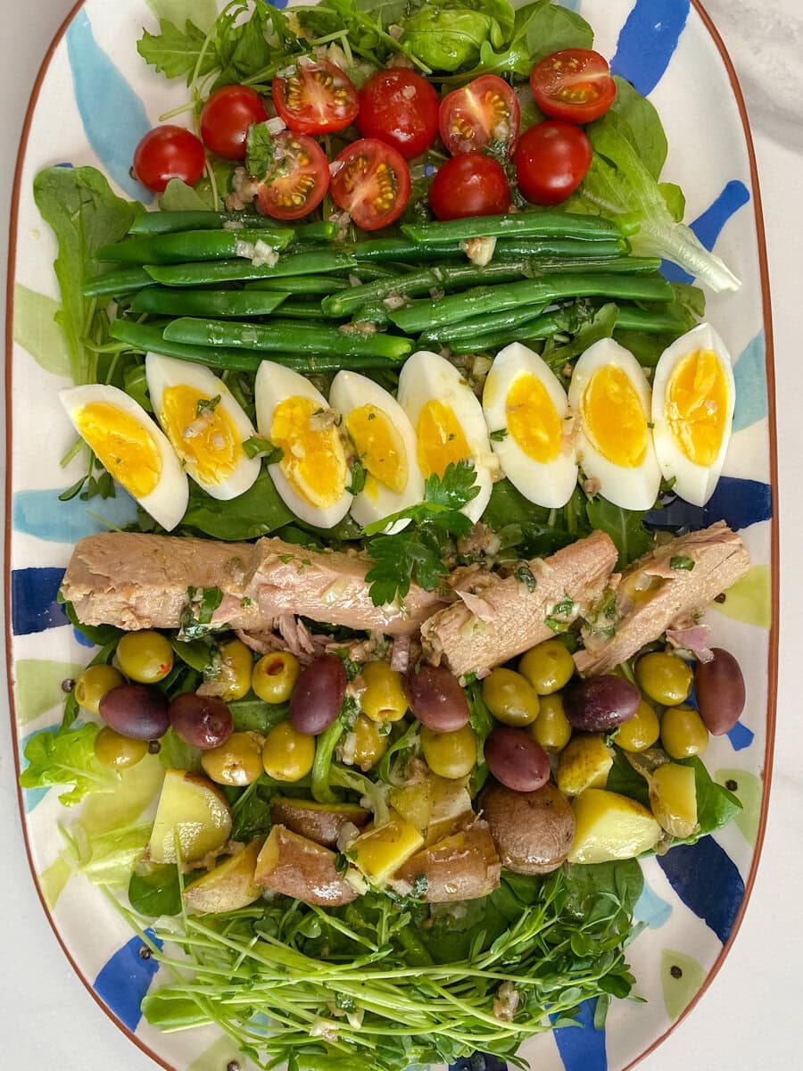 salade niçoise dans une grande assiette ovale, tomate, thon, oeufs, haricots, pommes de terre
