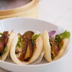 3 pain bao au porc dans un bol avec panier steamer en bambou en arrière plan