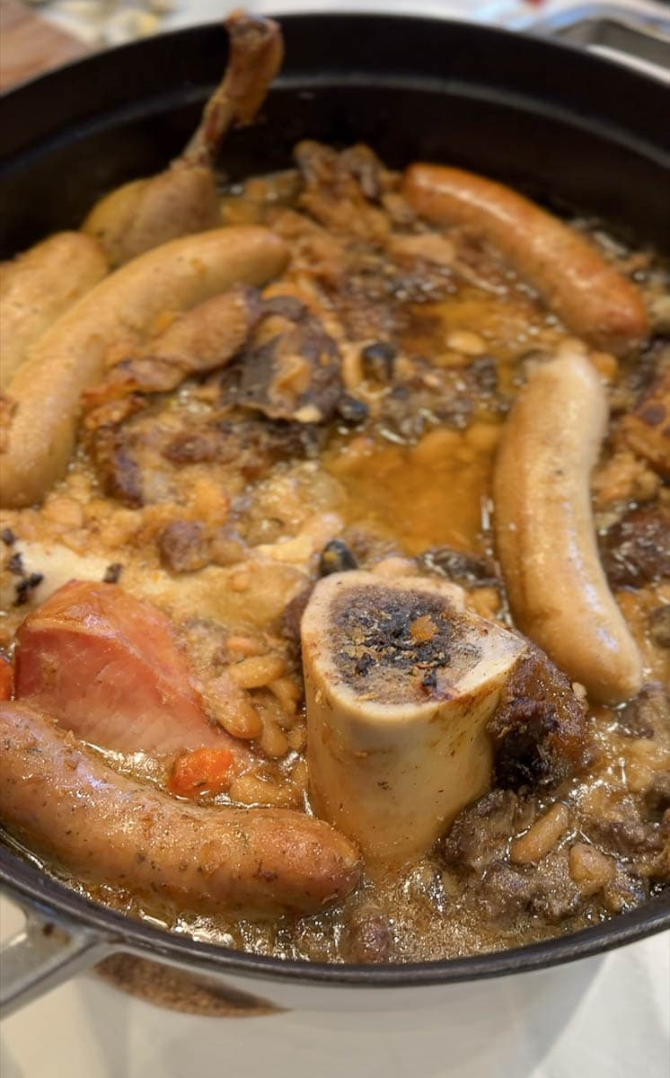 cassoulet avec saucisses, haricots, os à moelle, viande dans une grosse cocotte en fonte émaillée