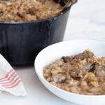 cassoulet maison dans un bol blanc, cocotte en fonte avec cassoulet visible en arrière plan