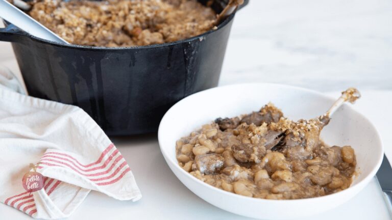 cassoulet maison dans un bol blanc, cocotte en fonte avec cassoulet visible en arrière plan