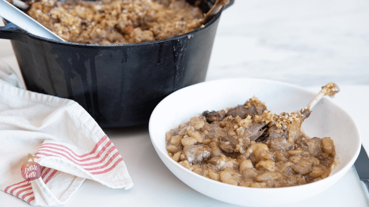 cassoulet maison dans un bol blanc, cocotte en fonte avec cassoulet visible en arrière plan