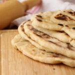 plusieurs pain naan maison grillé sur une planche de bois avec rouleau à pâtisserie en arrière plan
