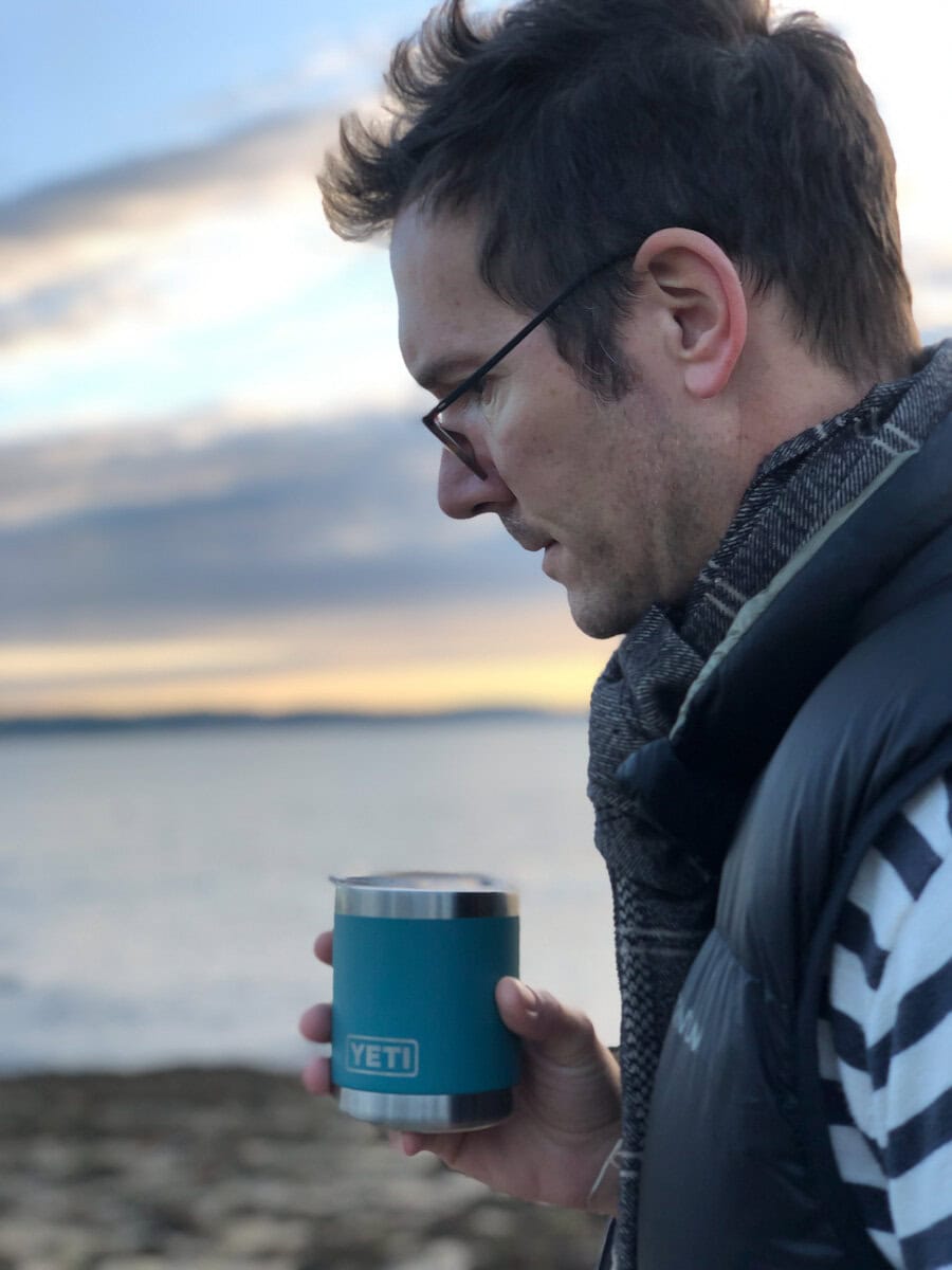 Lionel qui marche avec une tasse à café Yeti dans la main devant la mer