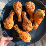 pilons de poulet frit dans une assiette bleue tenue par une main