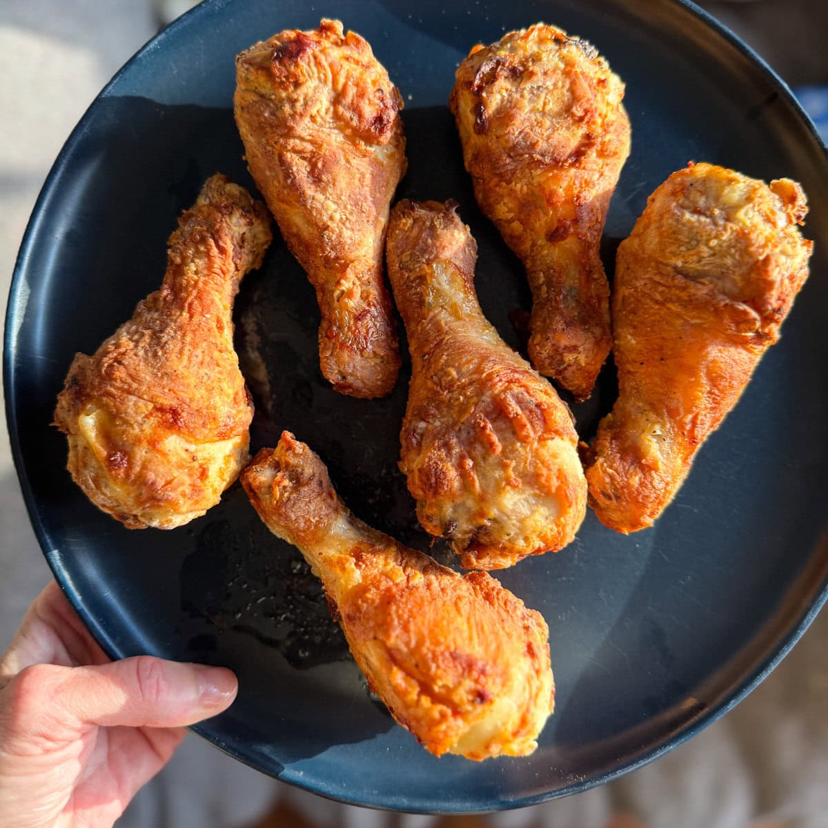 pilons de poulet frit dans une assiette bleue tenue par une main
