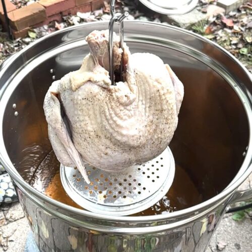 dinde entière non cuite qui plonge dans casserole d'huile