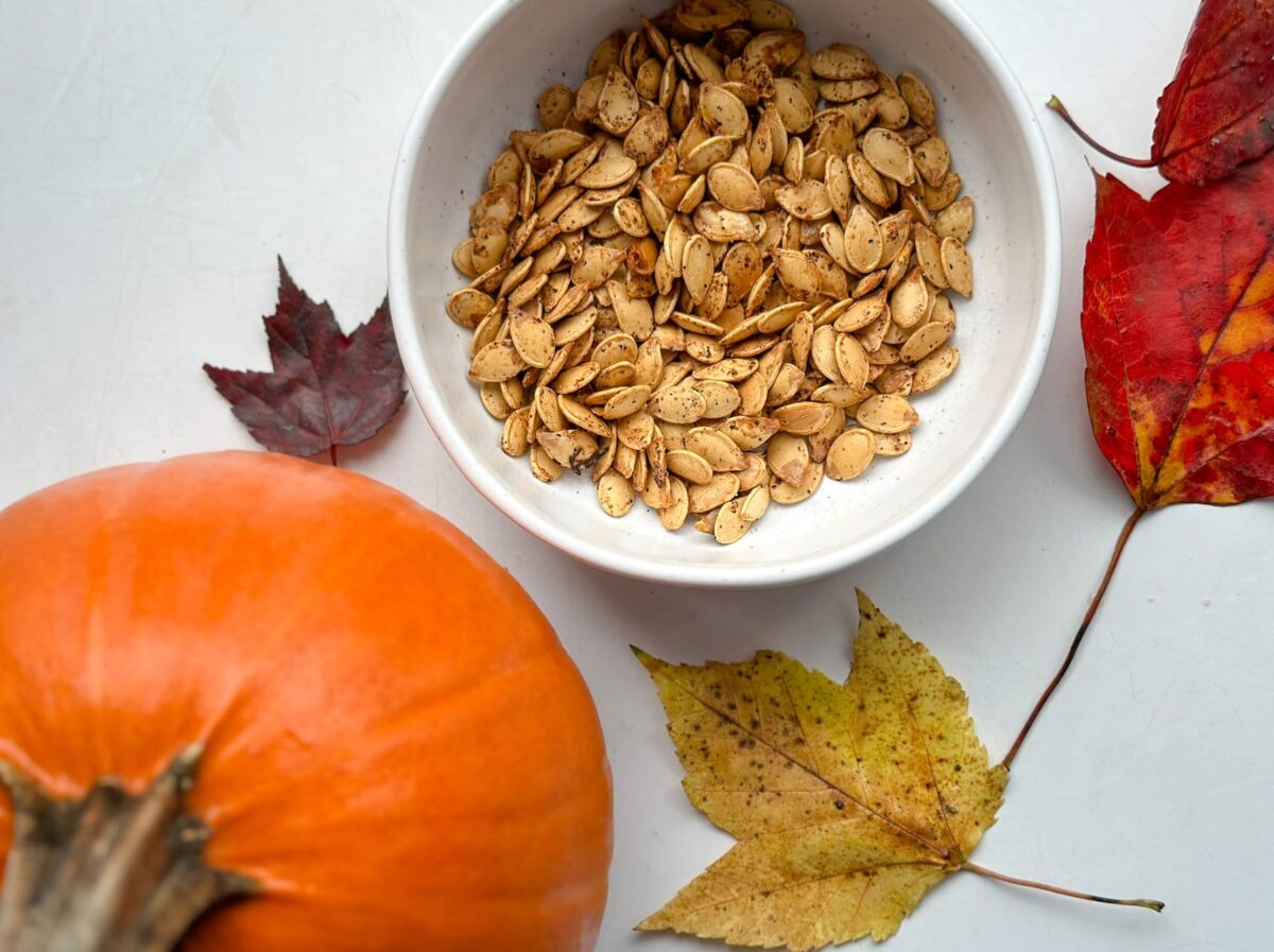graines de citrouille grillées dans un bol avec une petite citrouille et feuilles d'automne