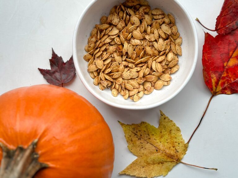 graines de citrouille grillées dans un bol avec une petite citrouille et feuilles d'automne