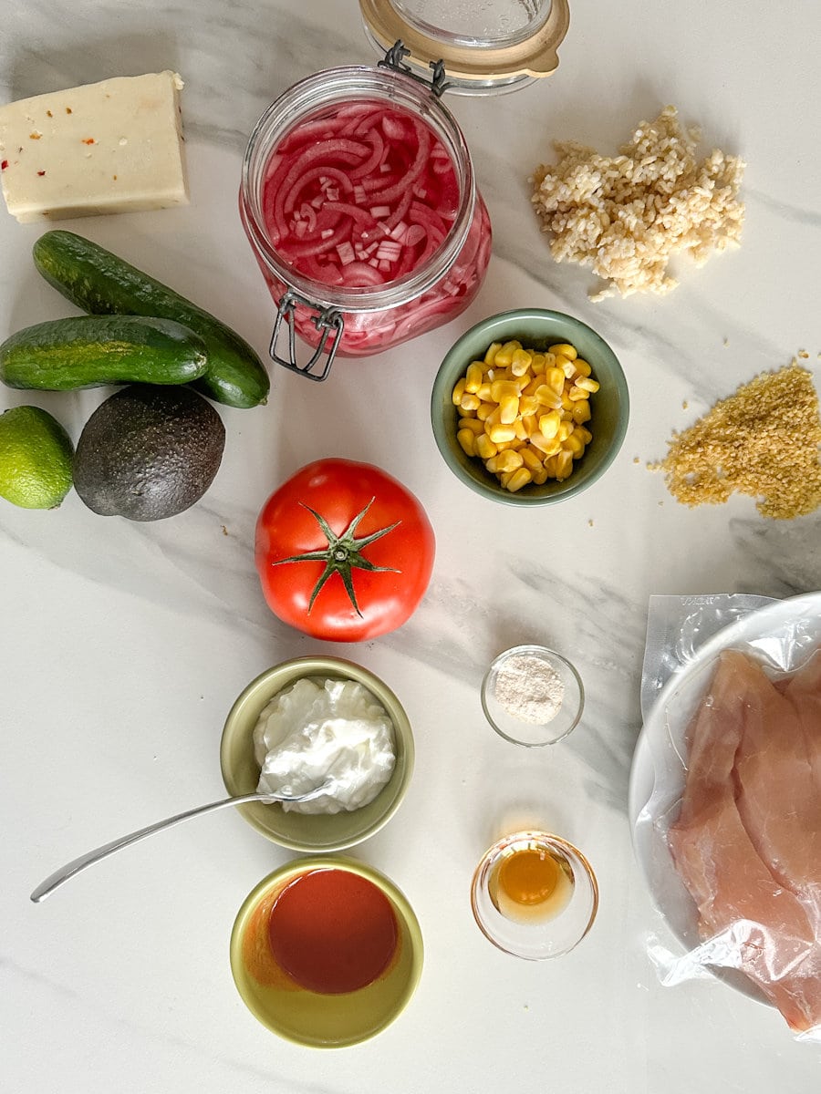 ingrédients dans bol poulet rouge: concombre, tomate, oignon, maïs, riz, poulet, marinade