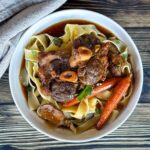 osso bucco porc avec carottes sur parpadelle dans une grand bol sur table en bois