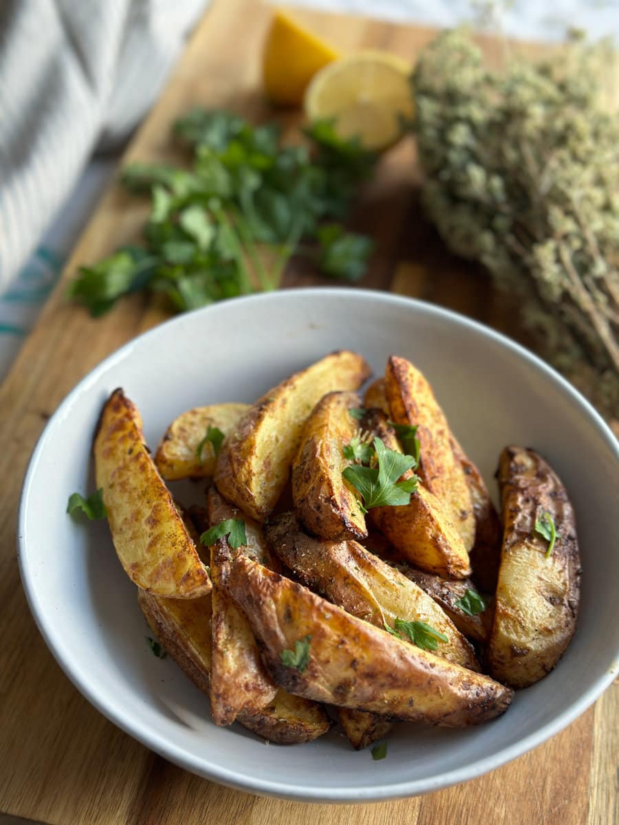 patates grecques grillées au air fryer dans un bol avec herbes sur planche de bois