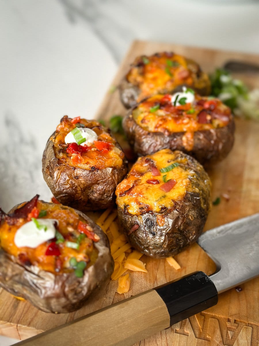 pomme de terre farcie toute garnie, au fromage, bacon, oignons verts sur une planche 