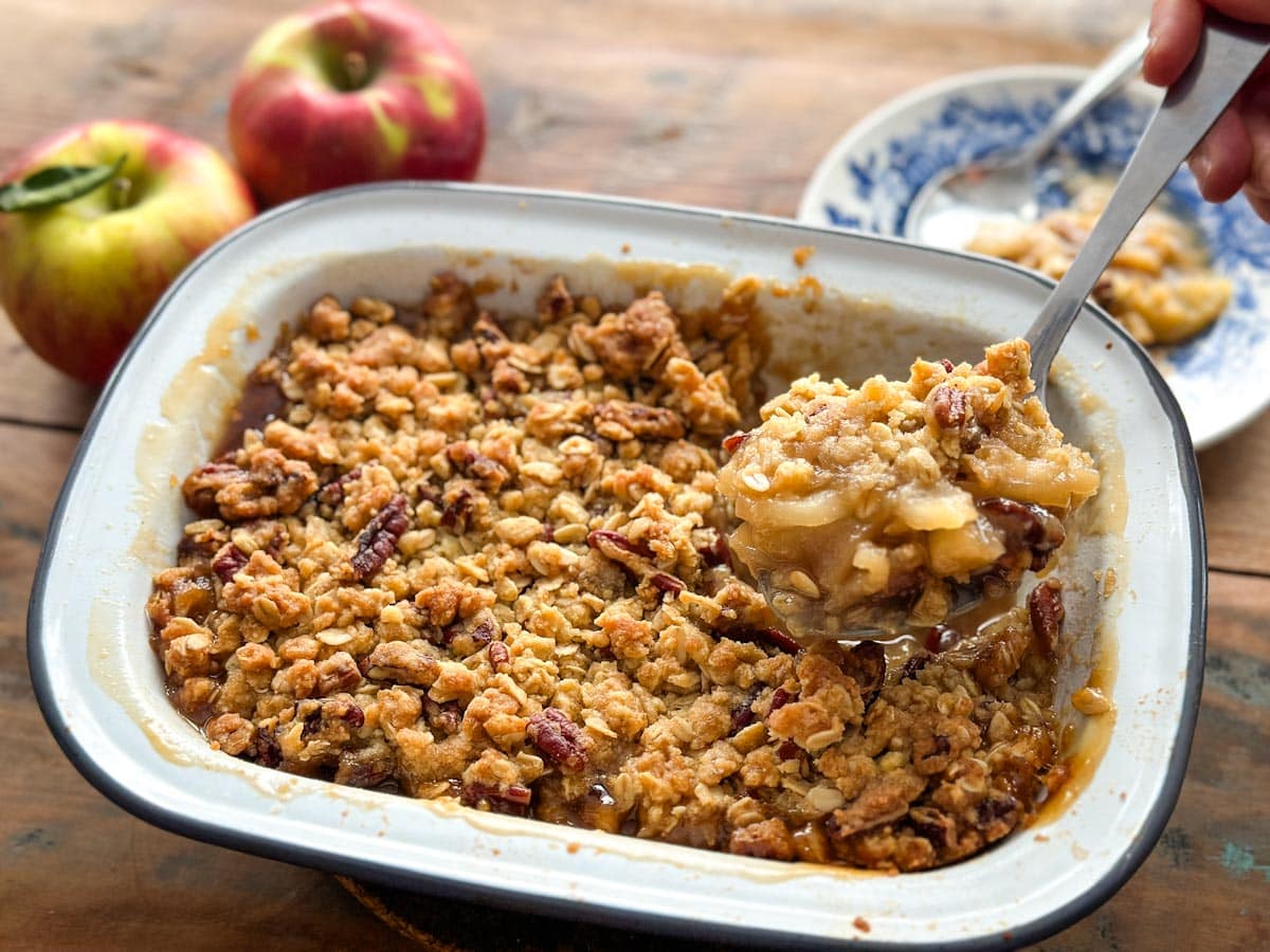 croustade aux pommes et érable dans un plat, avec cuillère de service et pommes en arrière plan