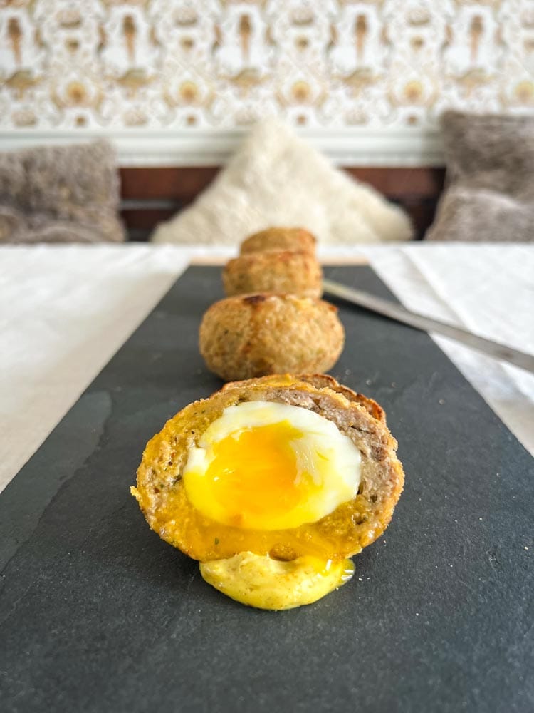 3 oeufs écossais sur planche de service, le premier ouvert au centre, jaune coulant sur sauce mayonnaise cari