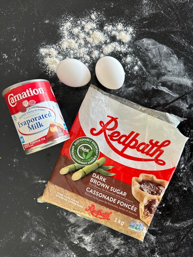 ingrédients pour tarte au sucre sur le comptoir: farine, oeufs, lait évaporé, cassonade foncée