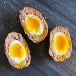 3 oeufs écossais (scotch eggs, jaune coulant, grillés sur planche de service en ardoise avec fleur de sel