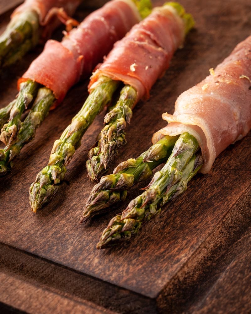 asperges grillées entourées de prosciutto sur une planche en bois