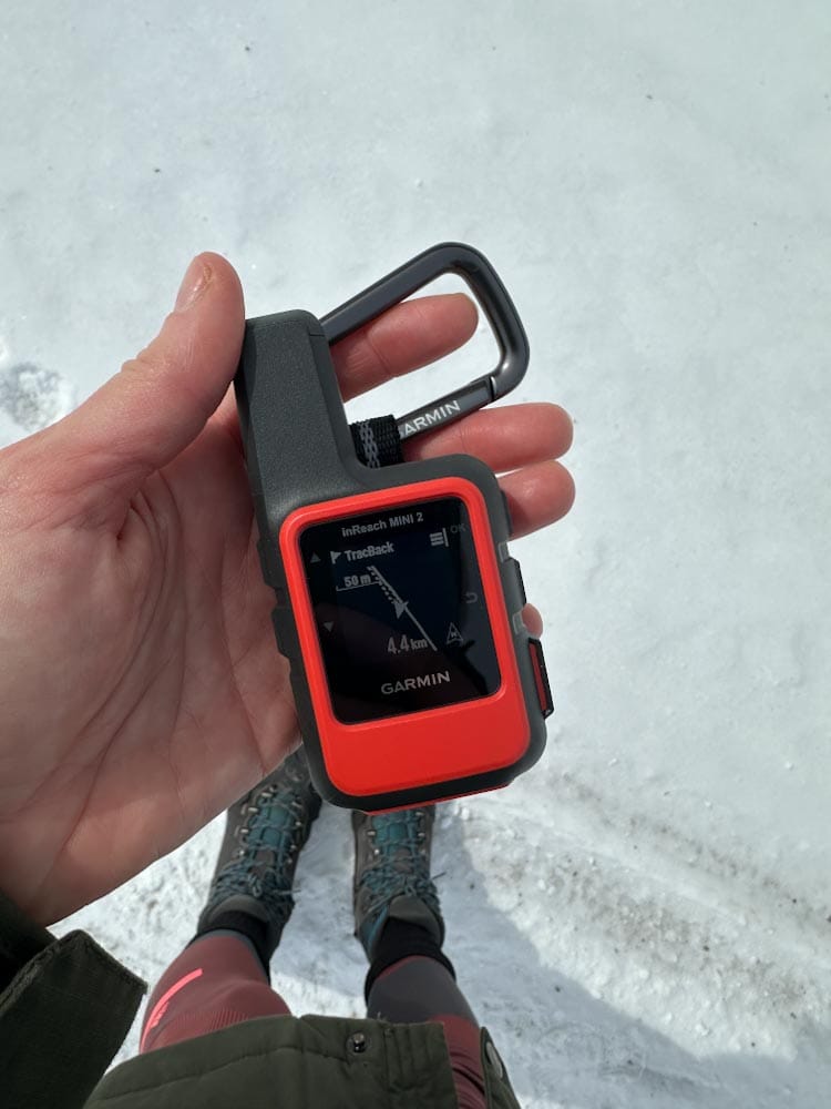 garmin in reach mini 2 dans la main, vue sur bottes de randonnée et neige