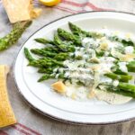 asperges vinaigrette avec copeaux de parmesan, dans une assiette et blocs de parmesan sur la nappe