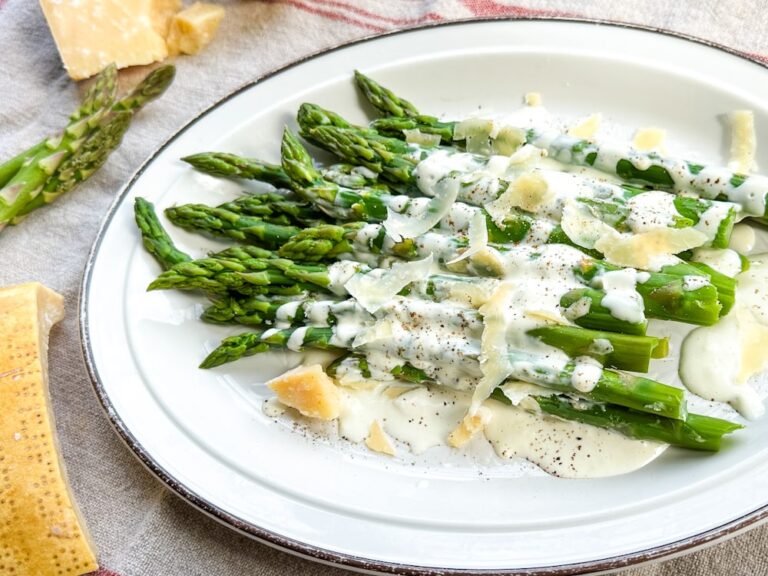 asperges dans une assiette blanche, recouverte de sauce blanche vinaigrette avec copeaux de parmesan et poivre