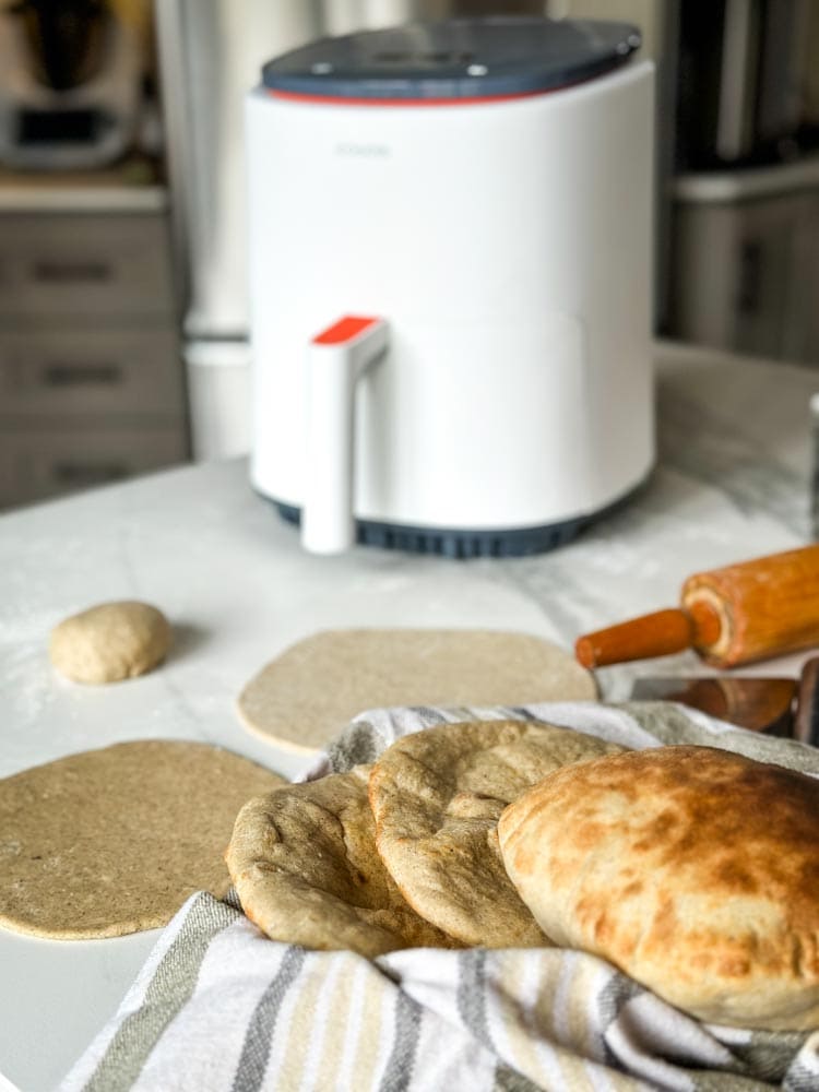 plusieurs pains pita cuits, pain non cuit en rond sur le comptoir, rouleau à pâtisserie et air fryer