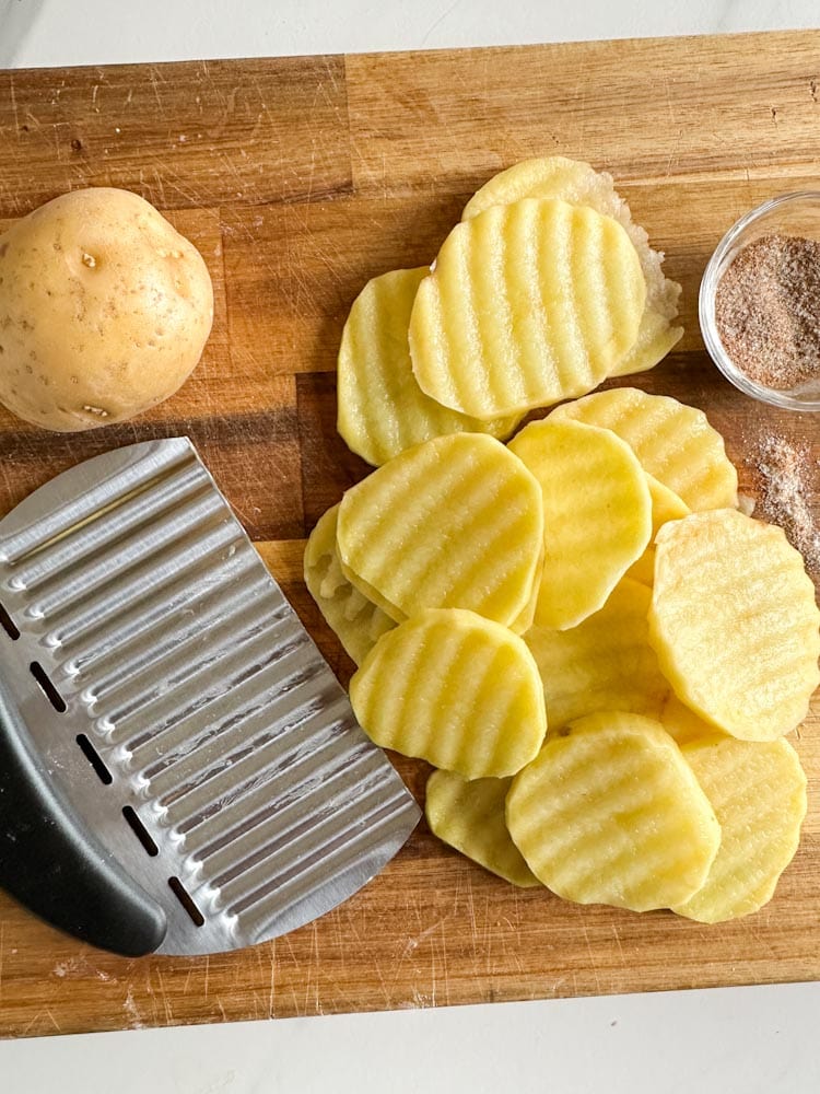 coupe pomme de terre ondulé sur une planche avec rondelles de patate gaufrée, pomme de terre et assaisonnement