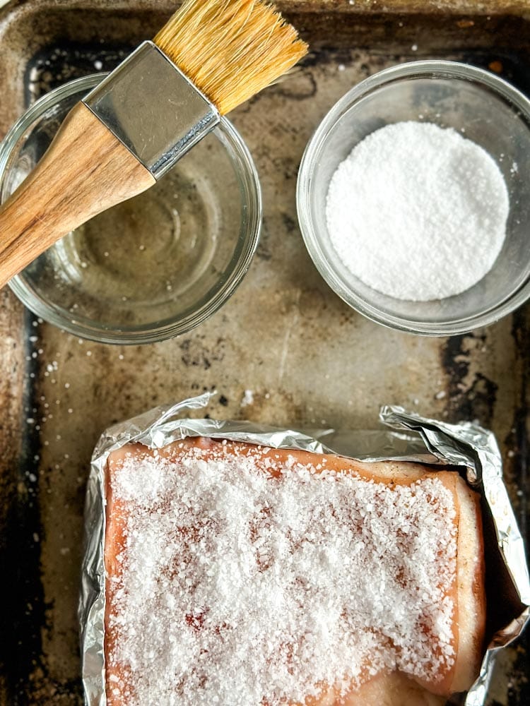 flanc de porc couvert de sel, pinceau dans le vinaigre et bol de sel marin