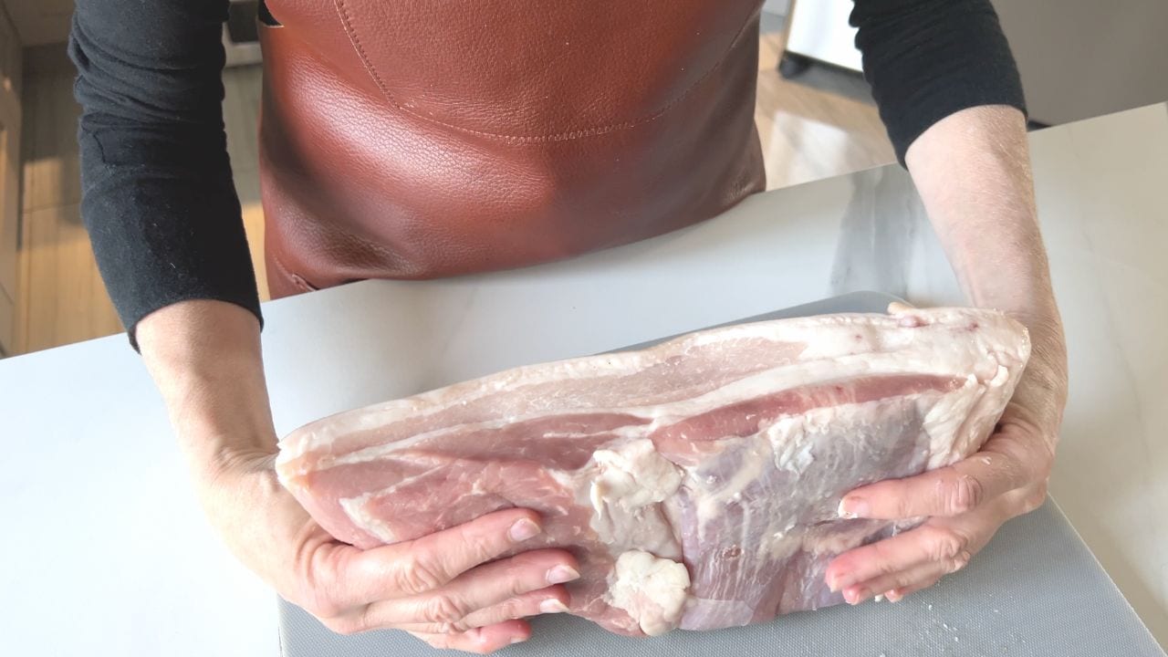 mains de femme qui tiennent la pièce de poitrine de porc crue