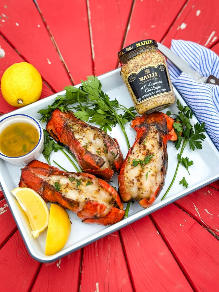 queues de homard grillées avec citron, moutarde Maille et persil frais sur une table rouge