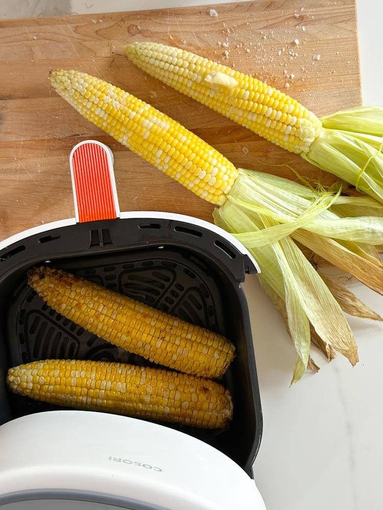  4 épis de maïs, deux vapeur avec feuilles sur planche et deux dans panier air fryer