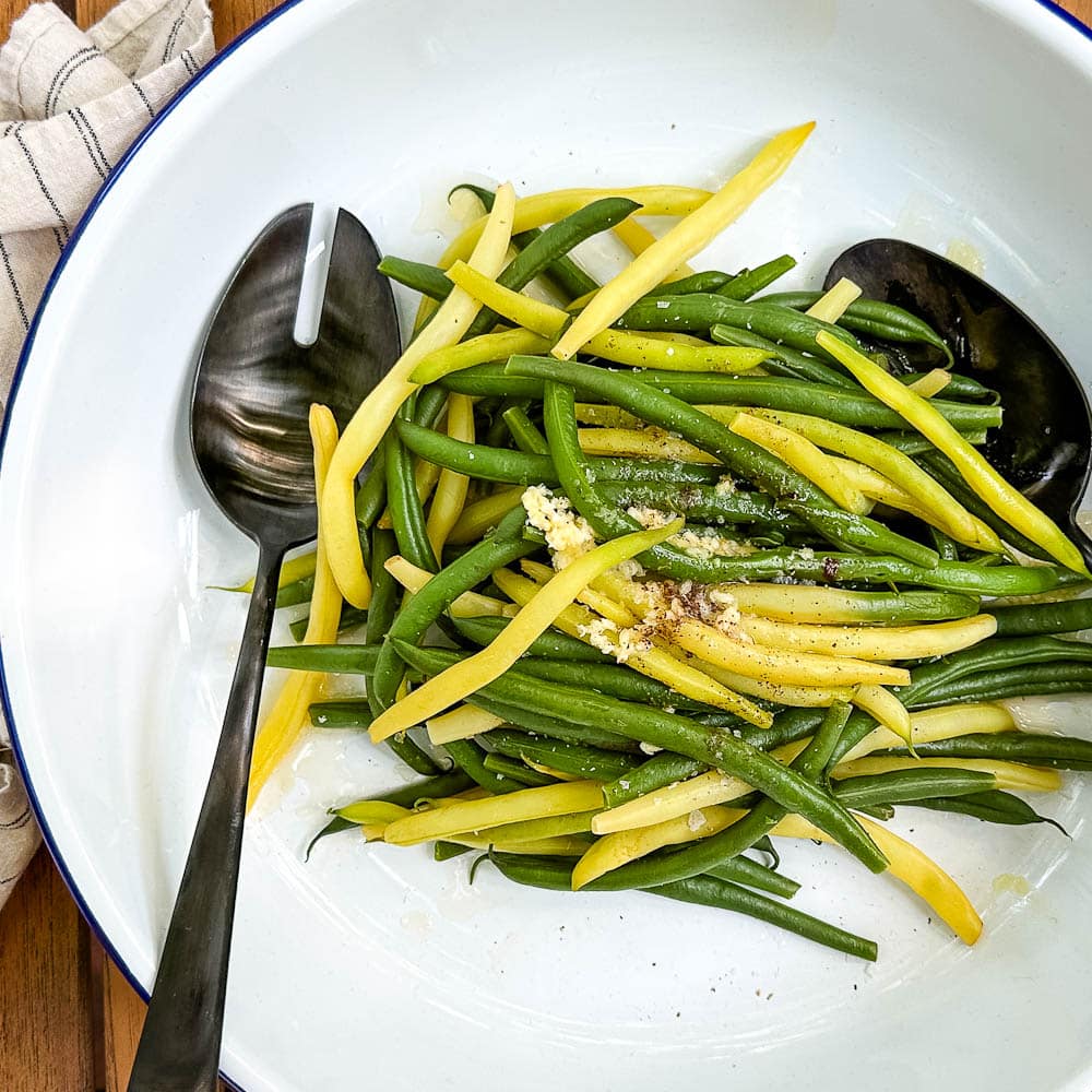 haricots verts et jaunes avec ail et beurre dans plat de service blanc avec cuillères noires