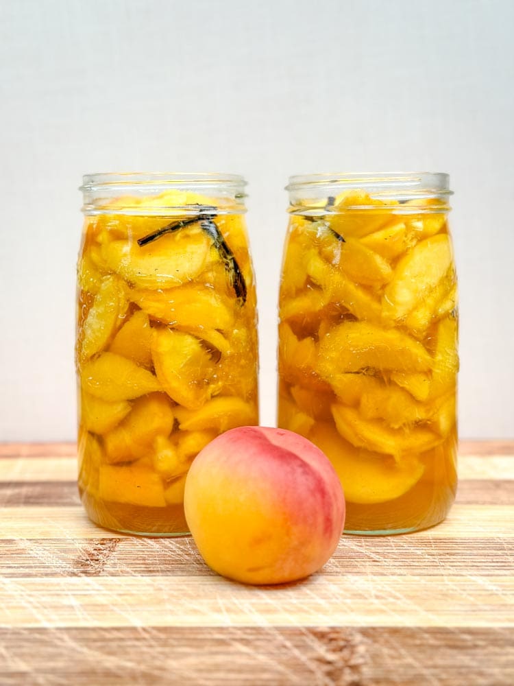 2 pots de conserve avec pêches dans le sirop à la vanille et pêche fraîches devant