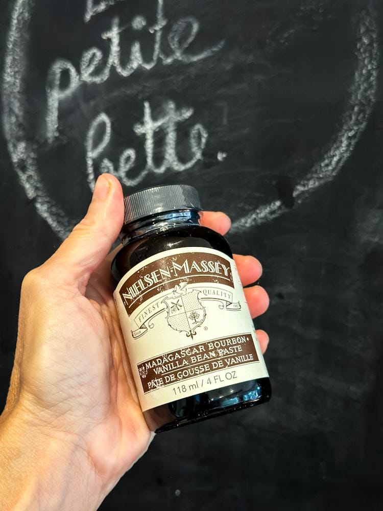 Pâte de gousse de vanille  Nielsen Massey dans la main devant ardoise Bette