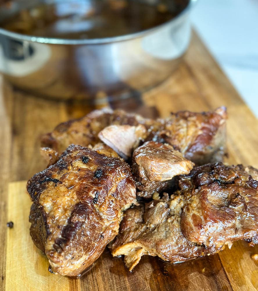 morceaux d'épaule de porc confit et grillé sur une planche avec casserole en arrière plan