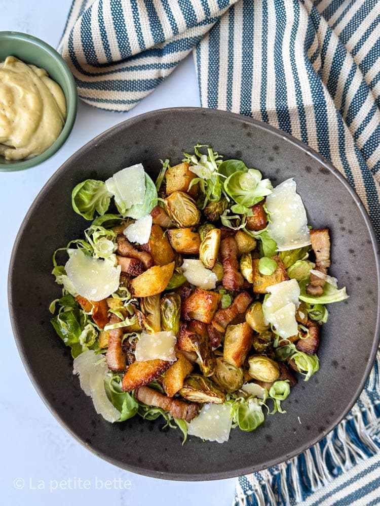 salade de choux de bruxelles style césar dans un bol noir avec vinaigrette césar à côté et linge de table