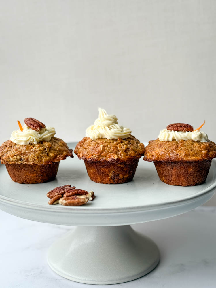 3 muffins aux carottes avec glaçage dans une assiette de service, avec noix de pacane