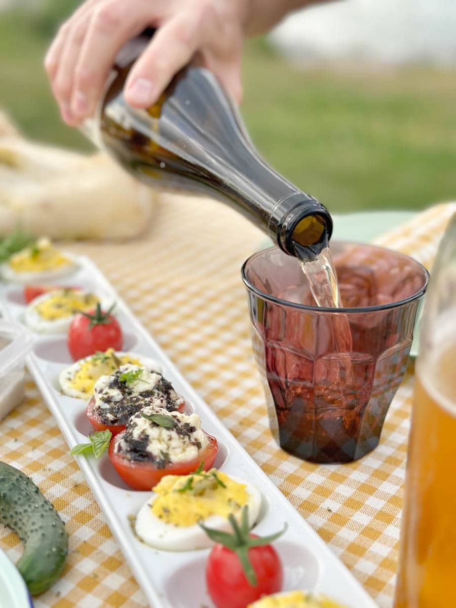 tablée pique-nique avec oeufs farcis mimosa, tomates farcies, verre de vin et une main qui tient la bouteille de vin