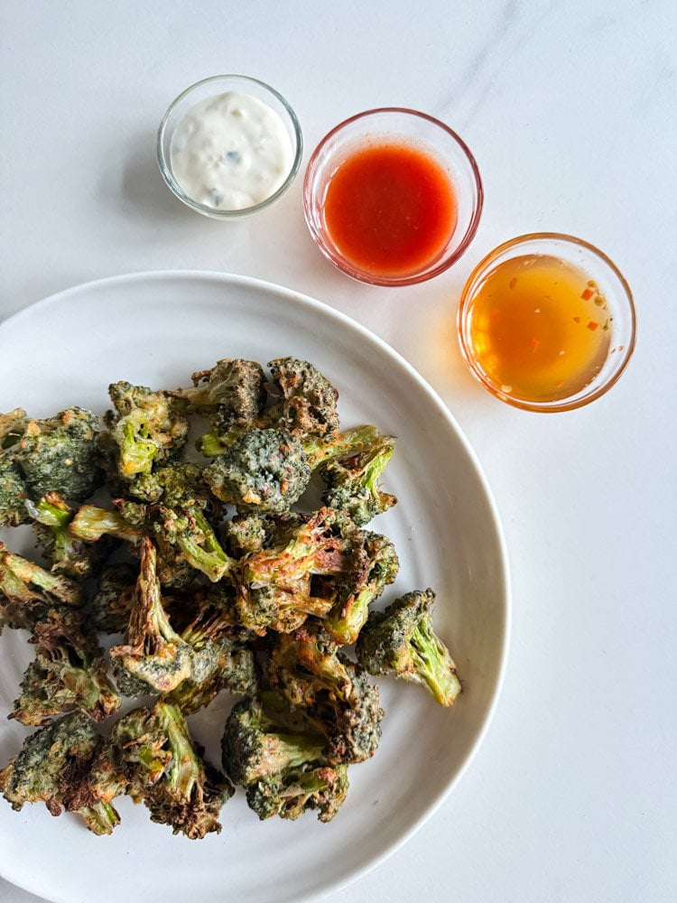 fleurons de brocoli grillés en panure dans une assiette blanche avec trois petits pots de sauce (blanche, rouge et liquide jaune)