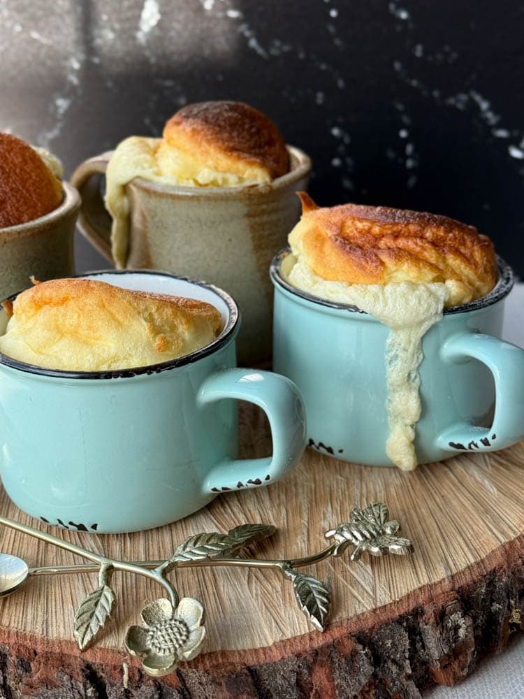 3 soufflés au fromage dans des tasses à café turquoise avec cuillères sur une planche en bois
