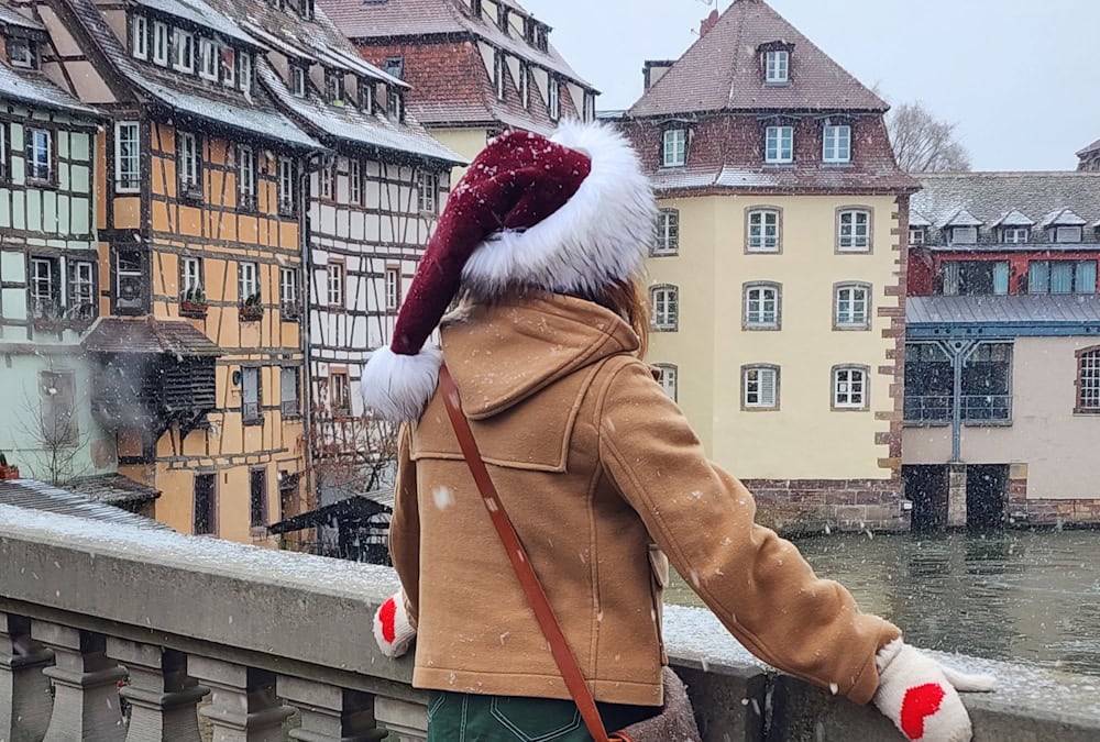 Manon Lapierre de dos avec chapeau de Noël devant maisons alsaciennes sous la neige