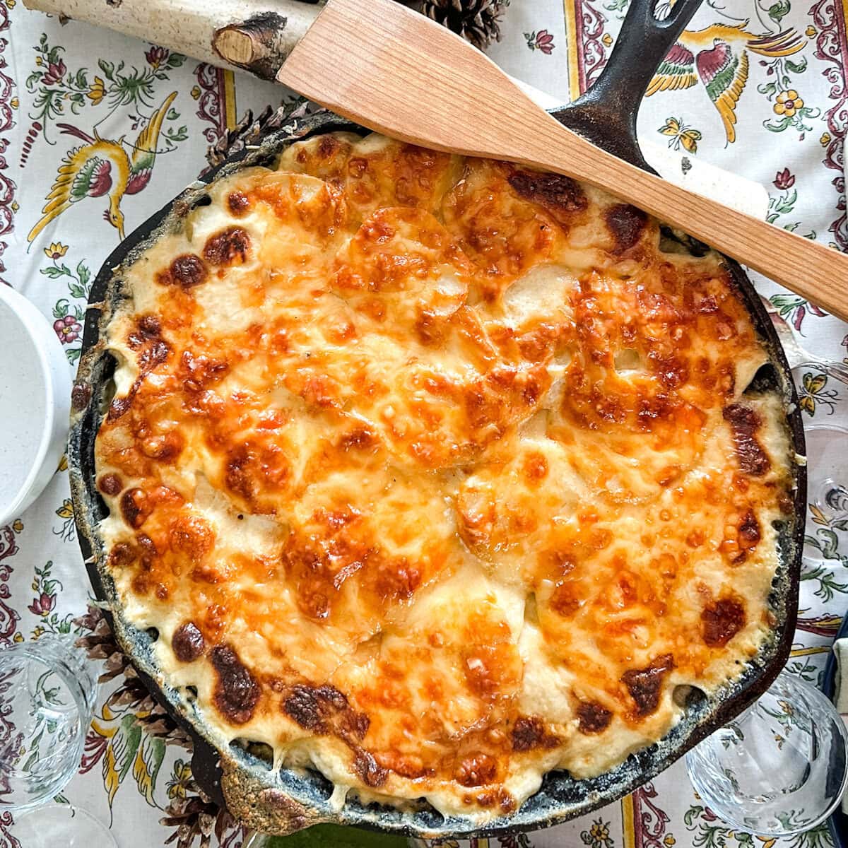 gratin dauphinois gratiné dans une grade poêle en fonte sur une table festive avec cuillère de bois