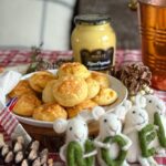 gougères au fromage et à la moutarde dans une assiette blanche, pot de moutarde Dijon maille en arrière plan, petites souris décoratives devant