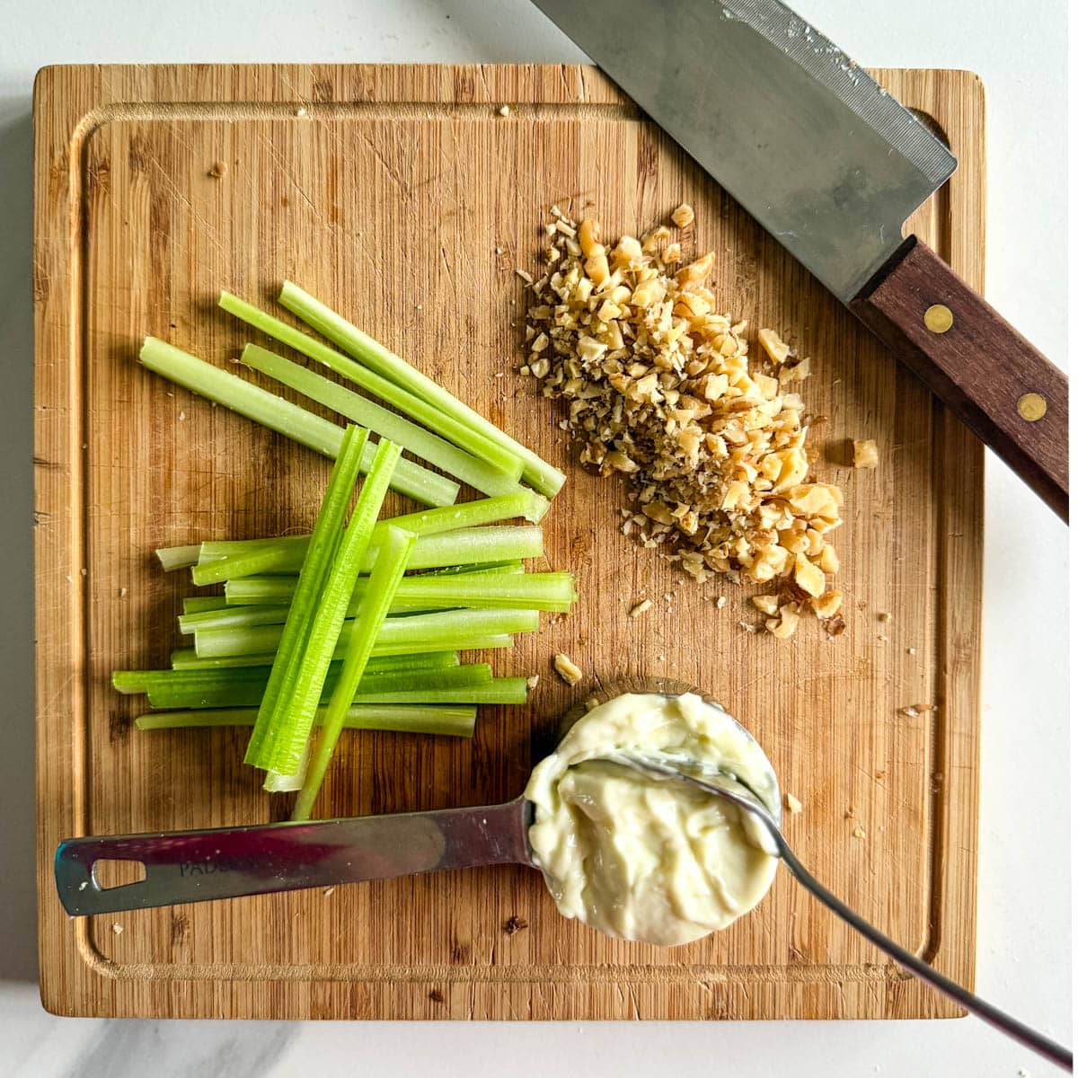 batonnets de céleri, noix hachées et petit pot de mayonnaise sur une planche avec couteau japonais