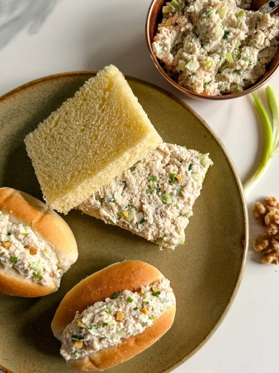 sandwich au poulet haché, deux petits pains fourrés un sandwich pas de croûte dans une assiette, oignon vert et noix sur le côté