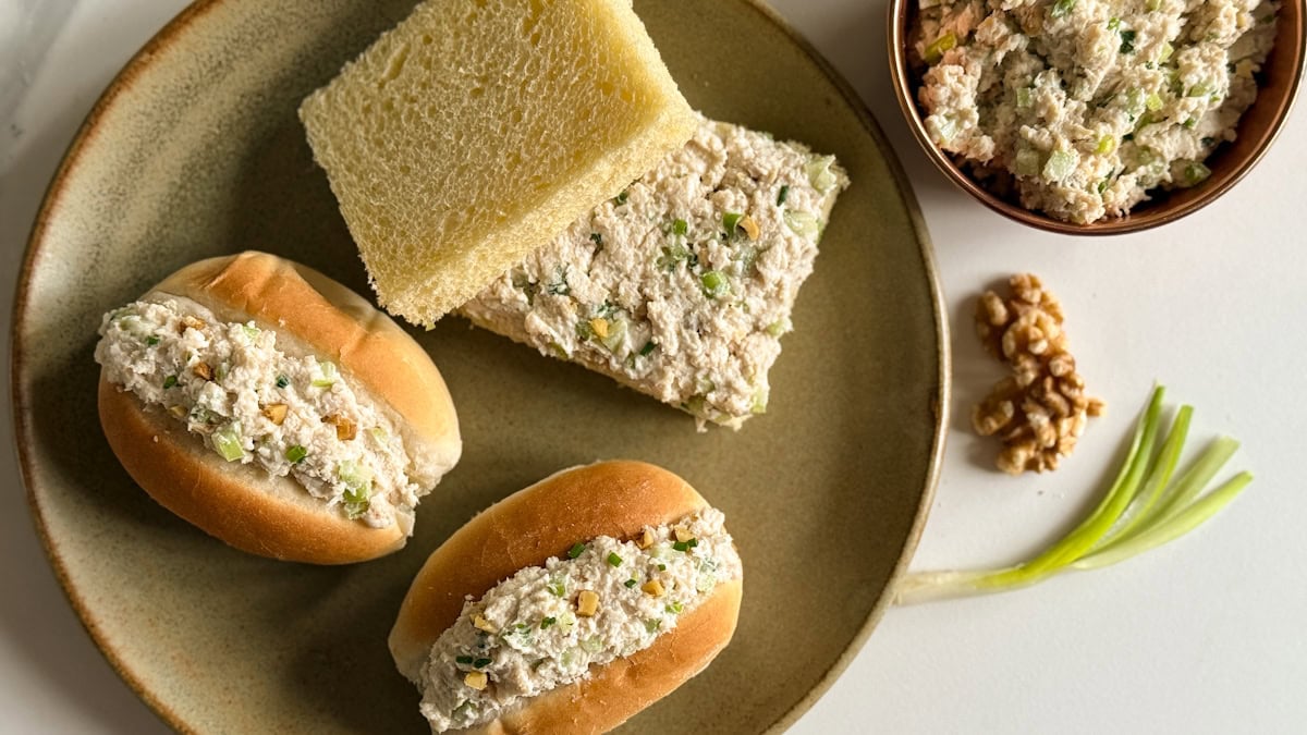 sandwichs au poulet dans une assiette, deux petits pains fourrés à la salade de poulet et une sandwich carrée, noix, céleri et oignon vert sur le comptoir à côté