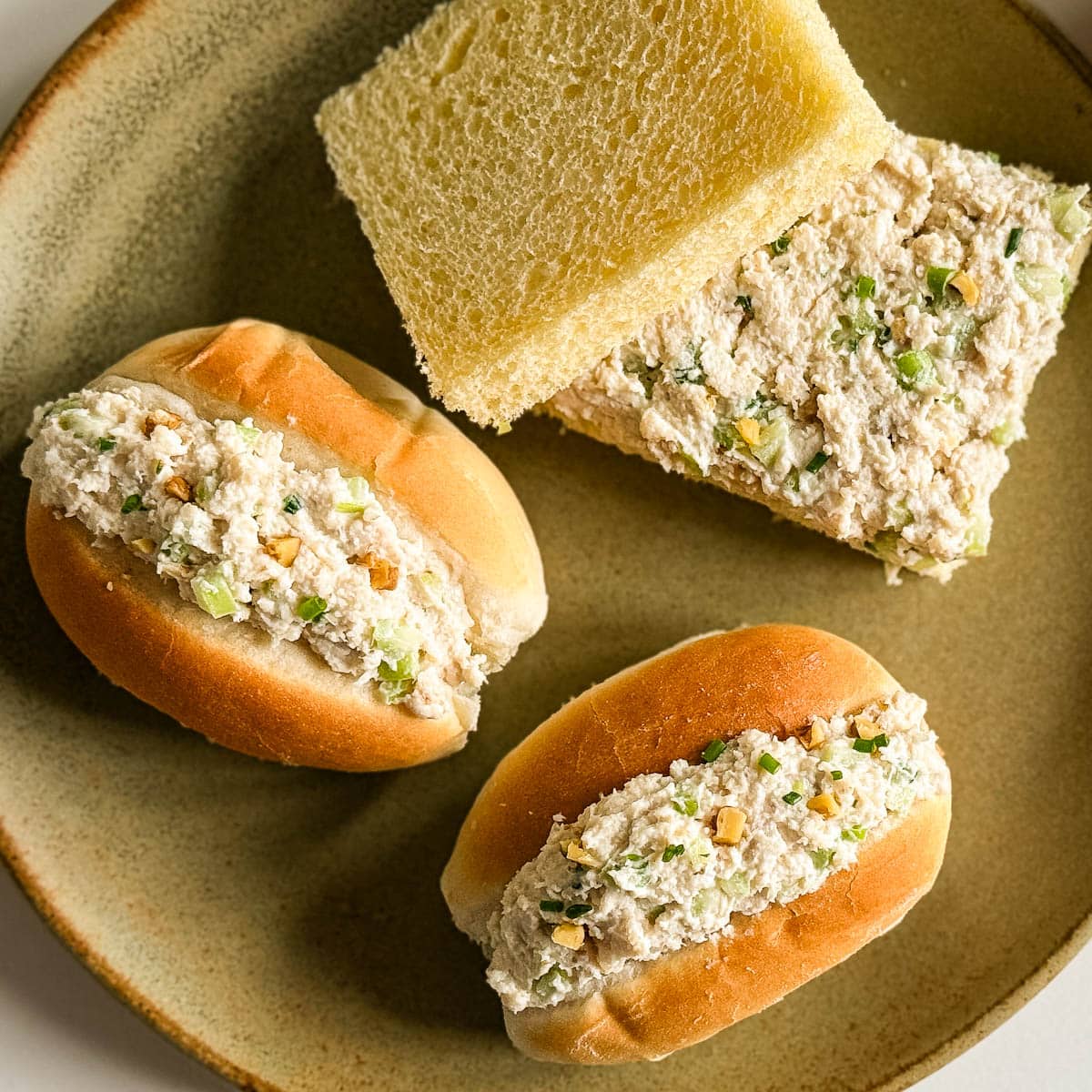 sandwich au poulet, 2 petits pains et un carré blanc sans croûte dans une assiette en grès